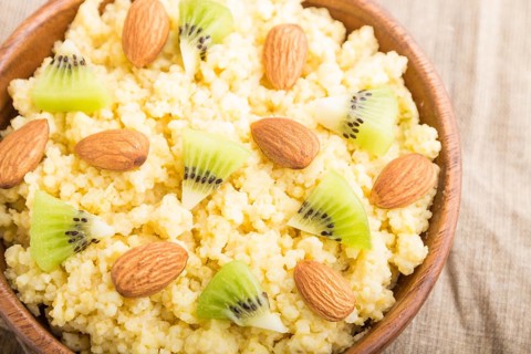 Millet porridge with kiwi and almonds in wooden bowl on a white wooden background and linen textile