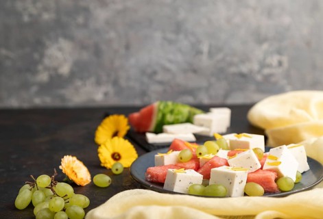 Vegetarian salad with watermelon, feta cheese, and grapes on blue ceramic plate on black concrete