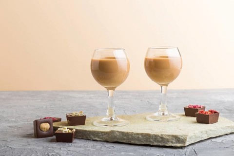 Sweet chocolate liqueur in glass with chocolate candies on a gray concrete background and stone