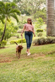 Vertical shot of a happy woman walking on the grass with her pet beside her outdoors. The woman is
