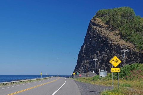 A road along a large cliff with a view of the sea and road signs indicating a cycle path, Gaspesie,