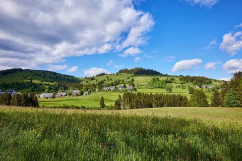 Landscape with hills, meadows, forests and a village under a blue sky with cumulus clouds near