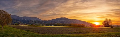Sunset over a wide landscape with fields and mountains in the background, pastel-coloured sky and