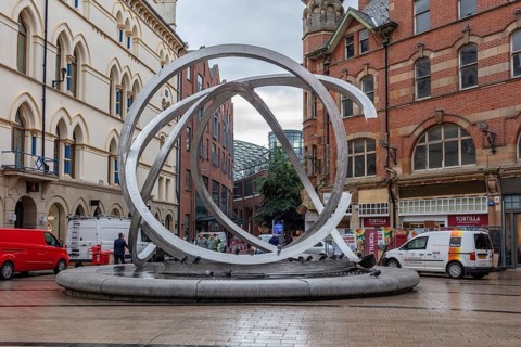 Modern sculpture in a busy street scene with people and buildings, Belfast