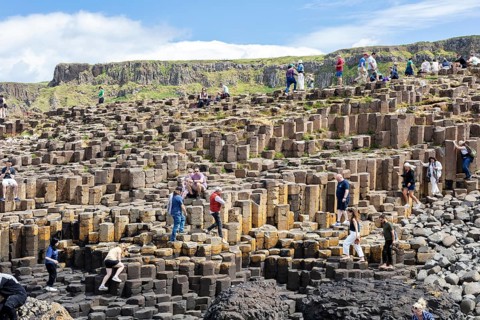 Tourists hike on staircase-shaped rock formations under a blue sky, Giant Causeway