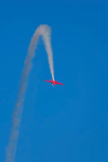 Red stunt aerobatic plane inverted flying loop performing stunts in blue sky. Concept of speed,