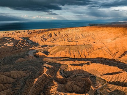 Riverbed runs through a landscape of eroded hills, badlands at sunset, Issyk Kul Lake in the