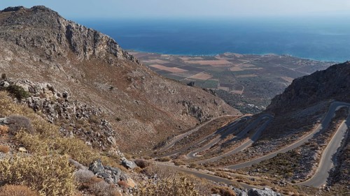Panorama of a winding road that stretches through hilly terrain to the coast and the blue sea,