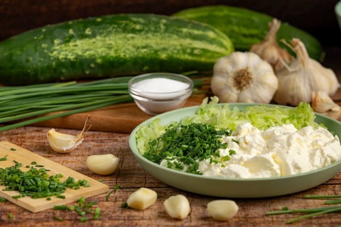 Fresh ingredients such as whole and grated cucumbers, garlic, chopped chives and sour cream on a
