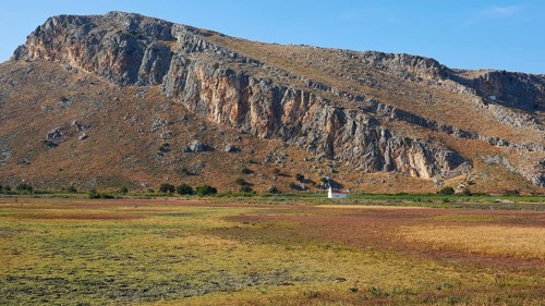 A small white chapel at the foot of a mountain surrounded by meadows, Strofilia biotope, wetlands,