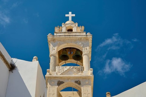 Close-up of a church tower with cross and bells under a bright blue sky, Platia and church Issodia