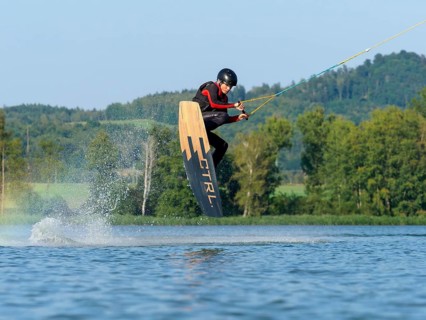 Young man jumping with wakeboard in lake, water sports, water skiing in wakepark, Stráž pod