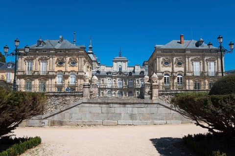 Baroque palace with symmetrical design and stone wall under a sunny sky, Royal Castle La Granja,