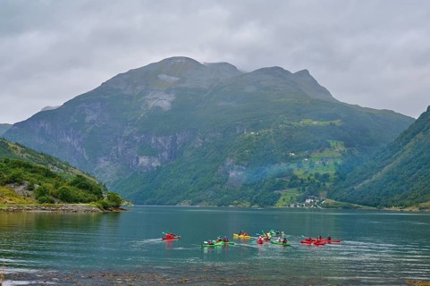 Several kayakers in a fjord surrounded by forested mountains and clouds, Geiranger, Geiranger