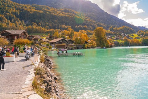 Picturesque lake with village, people on the shore and autumn trees in the background, Lake Brienz,