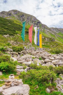 Scene in the mountains with colourful flags, a sign and green vegetation, surrounded by rocks,