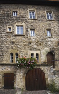 Old stone building facade with windows and decorated with colourful Pelargonium, Geranium flowers