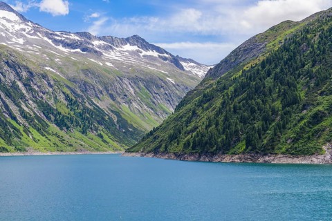 A peaceful mountain lake surrounded by green mountains, snow-capped peaks and a clear blue sky,