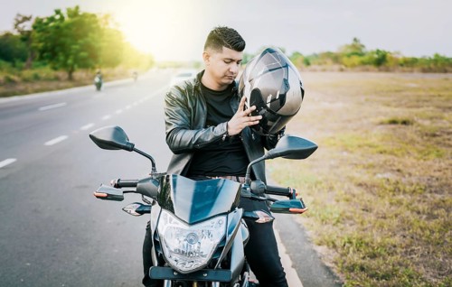 Young motorcyclist man putting on safety helmet outdoors. Male biker on motorcycle putting on
