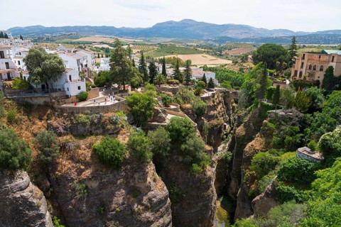 View of a dramatic gorge with a bridge surrounded by white buildings and green landscape in Ronda,