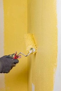Wall is painted with yellow paint, hand with paint roller