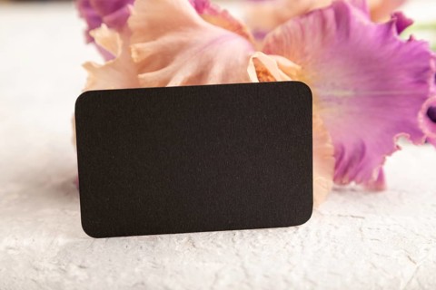 Black business card with iris purple flowers on white concrete background. side view, copy space,