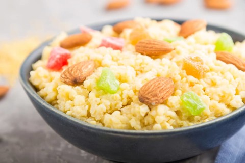 Millet porridge with candied fruits and almonds in blue ceramic bowl on a gray concrete background