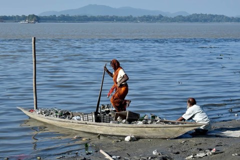 Rag picker collecting plastic bottle and other plastic materials in a boat from the bank of