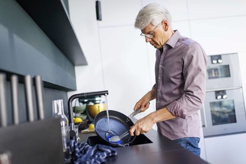 Symbolic photo. A man stands in the kitchen washing dishes. Berlin, 13.08.2024