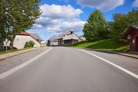 Bus stop Bernau Unterlehen, road and the chapel Unterlehen under a blue sky with cumulus clouds in