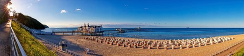 Sunlit beach with pier and historic building by the sea under a clear sky, Rügen, Sellin