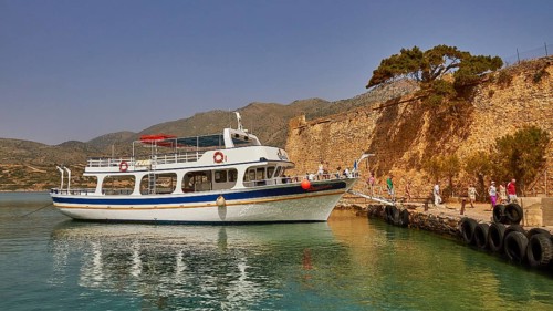 A boat moored in a quiet harbour next to a historic wall, with people on the jetty, Venetian Sea