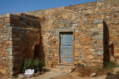Old stone house with a blue door surrounded by historical ruins and a flowering bush, Venetian Sea