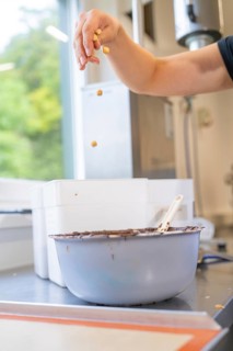 Hand sprinkles nuts into a bowl coated with dark chocolate, Burch Schokolade production,