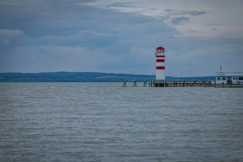 Red and white lighthouse stands on a calm lake under a cloudy sky, Podersdorf, Burgenland, Austria,