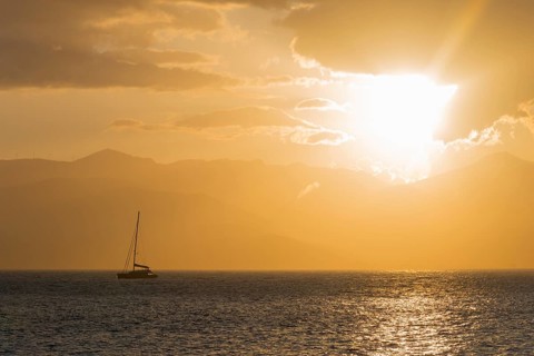 A sailboat on a calm sea at sunset with a golden sky and mountains in the background, Agia Kyriaki,