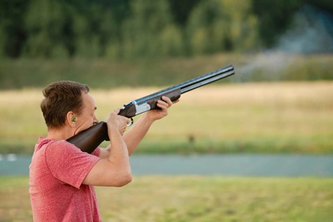 An old man shoots from a hunting rifle at a shooting range. Smoke from the barrel is visible in the