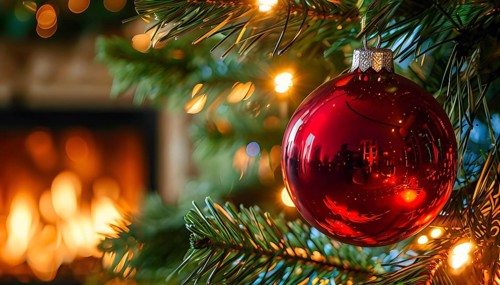 Christmas ornament hanging on a tree, with reflections of twinkling lights and fireplace flames