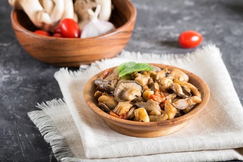 Fried oyster mushrooms with tomatoes in wooden plate on black concrete background. side view, close
