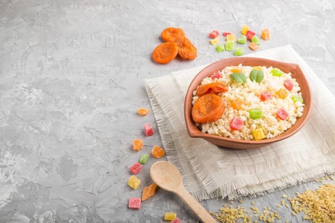 Bulgur porridge with dried apricots and candied fruits in clay bowl on a gray concrete background