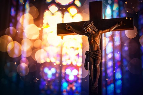Crucifix with Jesus Christ on cross in church with light coming through stained glass windows,