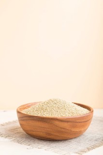 Wooden bowl with raw white quinoa seeds on a white and orange background and linen textile. Side