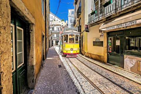 A vintage yellow tram navigates a narrow cobblestone lane in Lisbon, reflecting a sunny, vibrant
