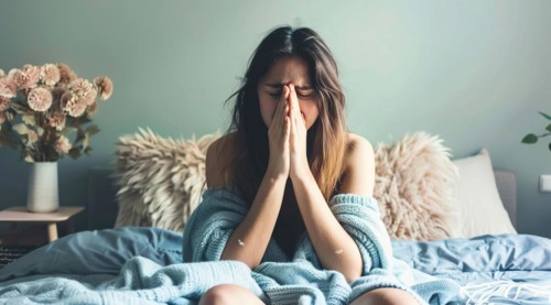 A woman lying in bed with a tissue in her hand, looking very sick with high temperature and fever,