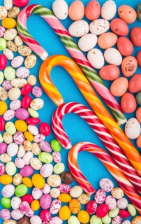 Colorful multicolored candies on a blue background. Christmas cane, chocolate eggs, caramel dragees