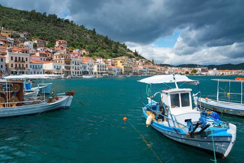 Harbour town with boats in the foreground and a forested range of hills in the background under a