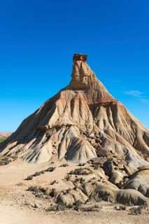 Steep rock formation in a dry desert landscape under a clear blue sky, Castildetierra, Bardenas