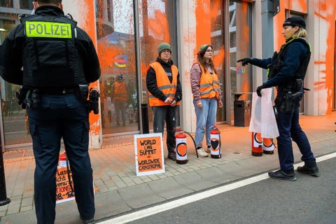 Police officer confiscates Last Generation banner after colour attack on Total Energies building.