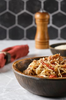 A flavorful dish of stir-fried noodles with colorful vegetables is presented in a rustic wooden