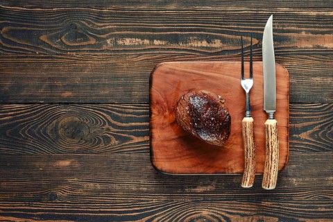 A beautifully grilled steak rests on a rustic wooden cutting board, accompanied by a knife and fork